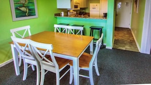 A dining area with a wooden table and white chairs, a kitchen with green walls and white cabinets, and a hallway leading to another room.