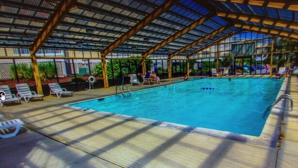 An indoor swimming pool with a covered roof, lounge chairs, and a poolside area.