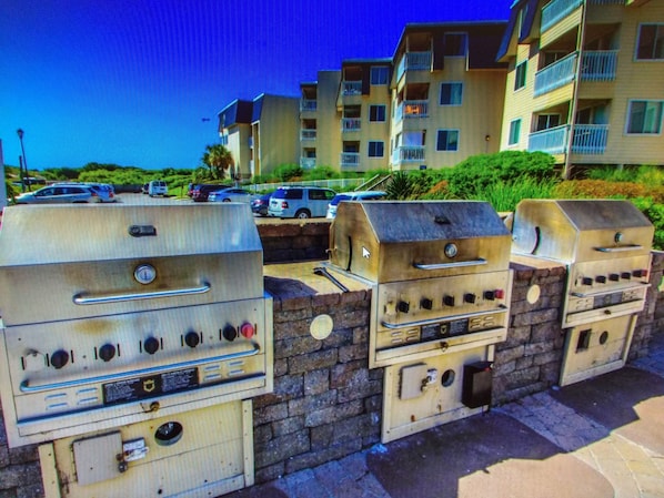 Outdoor barbecue grills, a stone wall, and a multi-story residential building with balconies.