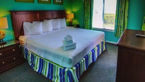 A hotel room with a large bed, a wooden headboard, a ceiling fan, and a window with curtains.
