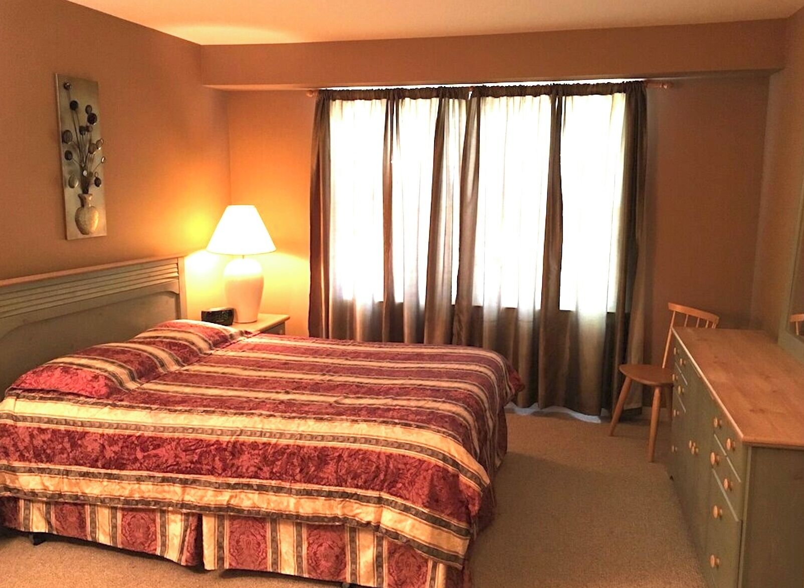 A hotel room with a bed, a desk, a chair, a lamp, and a window with curtains.