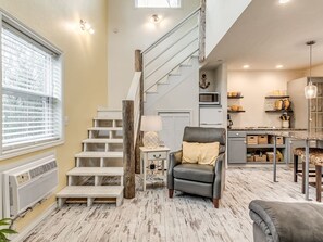A staircase with a wooden handrail, a gray leather chair, and a kitchen area with shelves and a dining table.