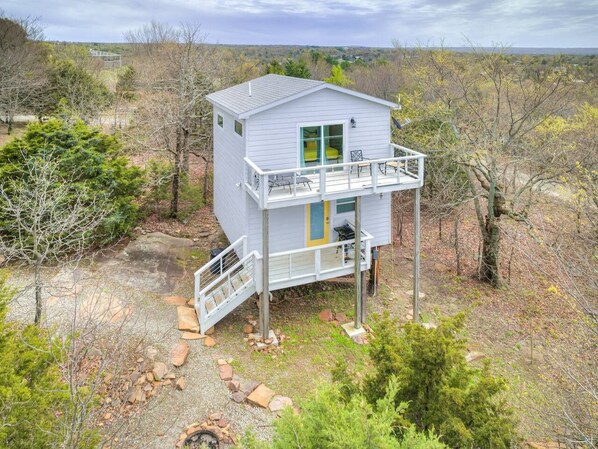 A single-story cabin with a balcony, surrounded by natural vegetation and a clear sky.