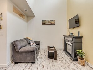 A living room with a grey sofa, a small table, a fireplace, and a mounted TV.