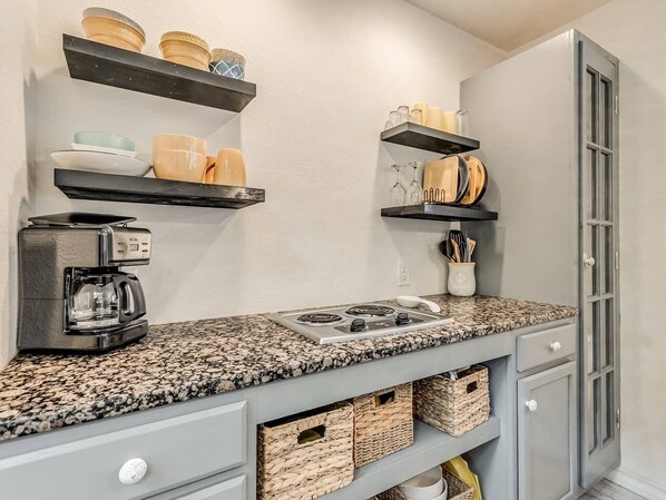 A kitchen with a granite countertop, a coffee maker, a stove, and storage baskets.