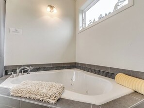 A bathroom with a large bathtub, a towel, and a wall-mounted light fixture.