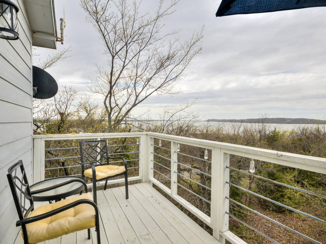 A deck with two chairs and a table, overlooking a body of water and trees.