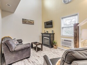 A living room with a fireplace, a sofa, a coffee table, and a television mounted on the wall. - Romantic Lakeview Treehouse with Jacuzzi Tub, Loft & Private Balcony (Stigler)