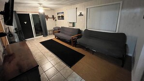 A living room with a sofa, a coffee table, and a TV mounted on the wall. There is a door leading to another room and a window with blinds. - Gilead Lakefront Cottage with Large Deck and Beautiful View (Bronson)