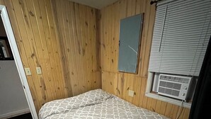 A small room with a bed, wooden walls, a window with blinds, and a wall-mounted air conditioning unit. - Gilead Lakefront Cottage with Large Deck and Beautiful View (Bronson)