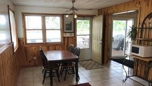 A dining area with a wooden table and chairs, a ceiling fan, and a view of the outdoors through large windows. - Gilead Lakefront Cottage with Large Deck and Beautiful View (Bronson)