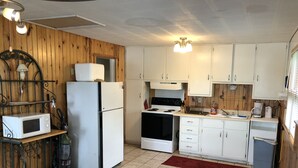 A compact kitchen with white cabinets, a stove, a microwave, and a refrigerator. There is a dining table with chairs and a red rug on the floor. - Gilead Lakefront Cottage with Large Deck and Beautiful View (Bronson)