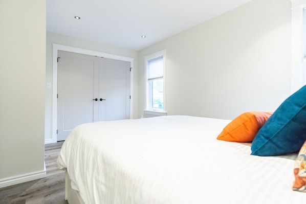 A bedroom with a large bed, white walls, a window, and a door.