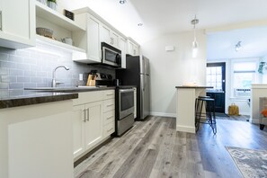 A modern kitchen with white cabinets, stainless steel appliances, and a wooden floor.