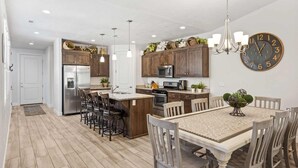 A modern kitchen with wooden cabinets, stainless steel appliances, and a dining area with a large table and chairs. - Desert Pearl at Paradise Village! Waterpark & Lazy River! (Santa Clara)