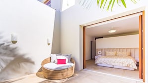 Quarto com uma cama, uma cadeira de vime e uma janela grande.