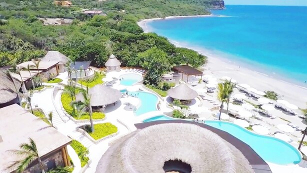 Um resort com área de piscina central, várias piscinas menores e uma praia.