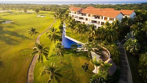 Campo de golfe com piscina, rodeado por palmeiras e um edifício grande com várias varandas.