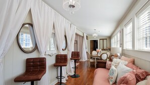Une pièce avec un plancher en bois, un canapé rose, des fauteuils en cuir marron, une table à manger avec des chaises et un grand miroir.