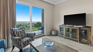 A living room with a large sliding glass door leading to a balcony, a television, and a patterned armchair.