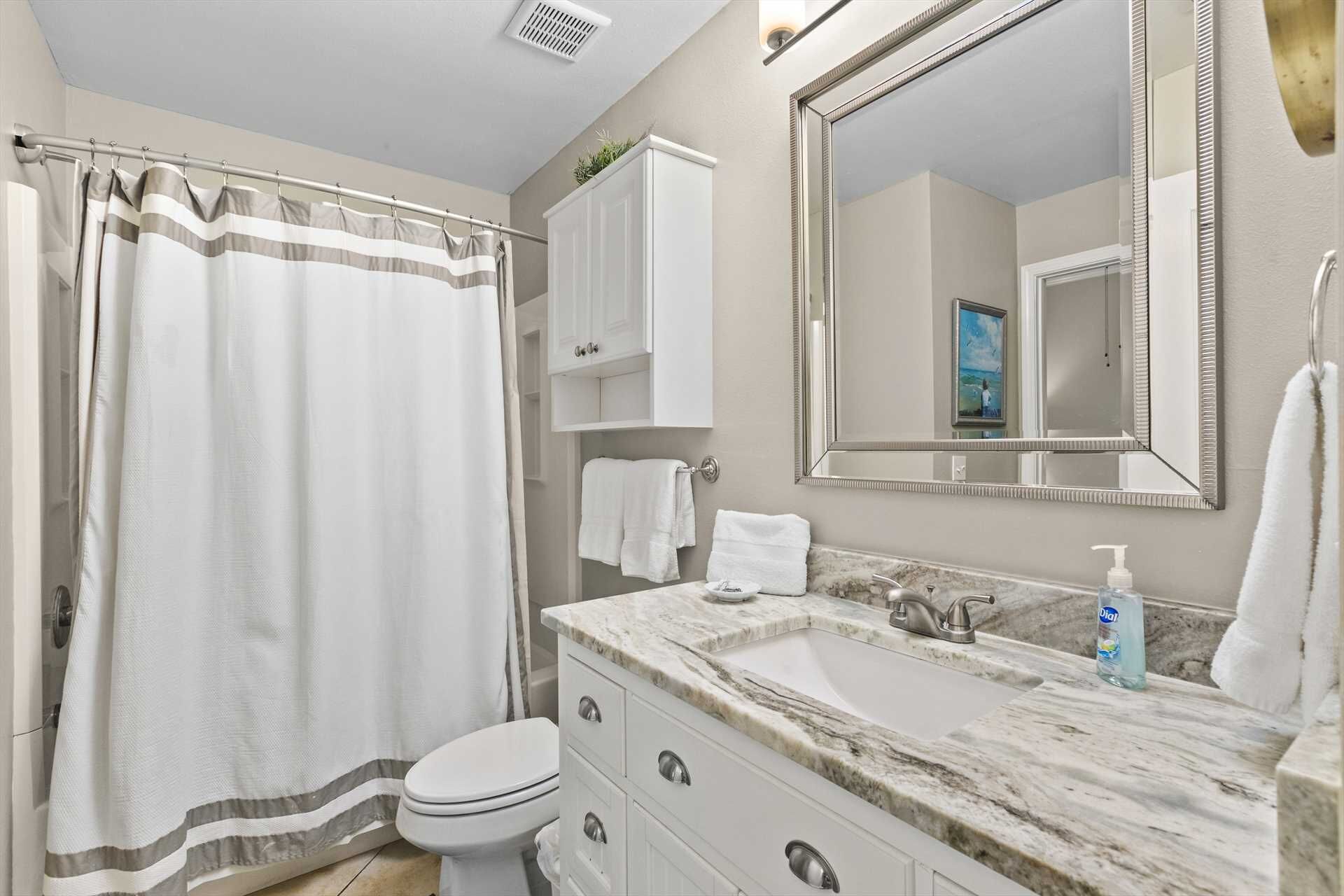 A bathroom with a shower curtain, toilet, sink with marble countertop, and a large mirror.