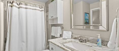 A bathroom with a shower curtain, toilet, sink with marble countertop, and a large mirror.