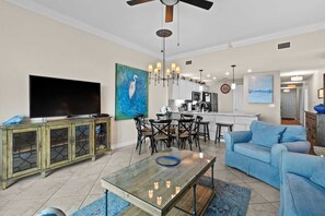 Una sala de estar con televisión, comedor, cocina y un sofá azul.