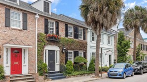 A row of brick townhouses with a red door, black shutters, and a blue car parked on the street. - Private Courtyard + Steps from King St +Parking Included (Charleston)