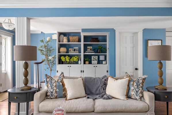 A living room with a beige sofa, two side tables with lamps, a bookshelf, and a door in the background.