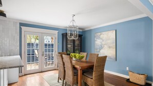 A dining area with a wooden table, wicker chairs, a chandelier, and a view through glass doors to an outdoor area. - Private Courtyard + Steps from King St +Parking Included (Charleston)