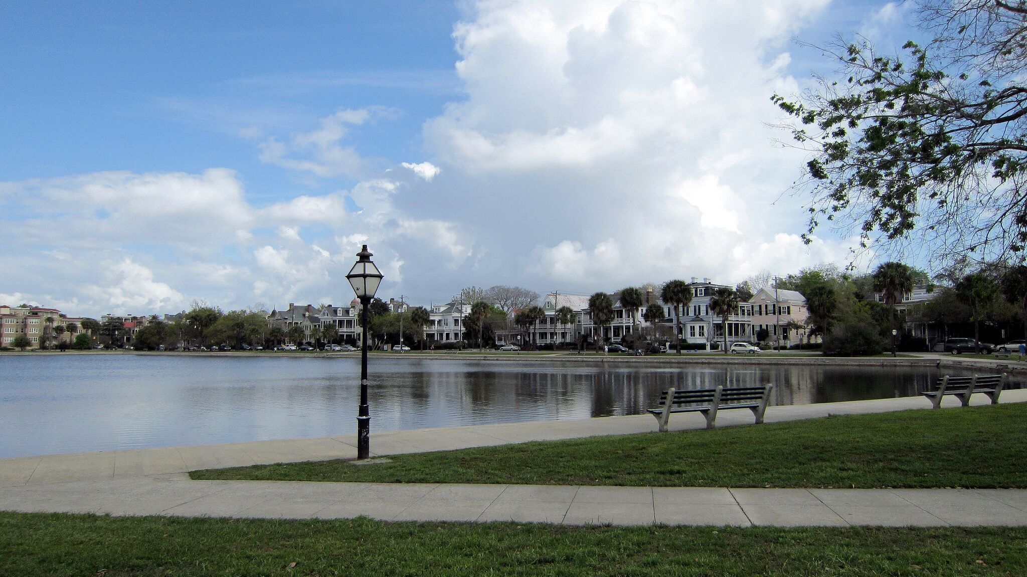 Un parque con un lago, bancos y un farol.