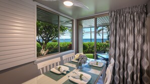 A dining area with a table set for four, a ceiling fan, and a view of the ocean through large windows.