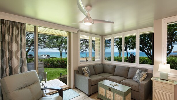 A living room with a view of the ocean, a ceiling fan, and a green chest of drawers.