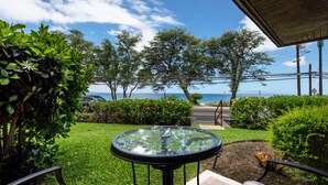 A patio with a glass table, chairs, and a view of the ocean.