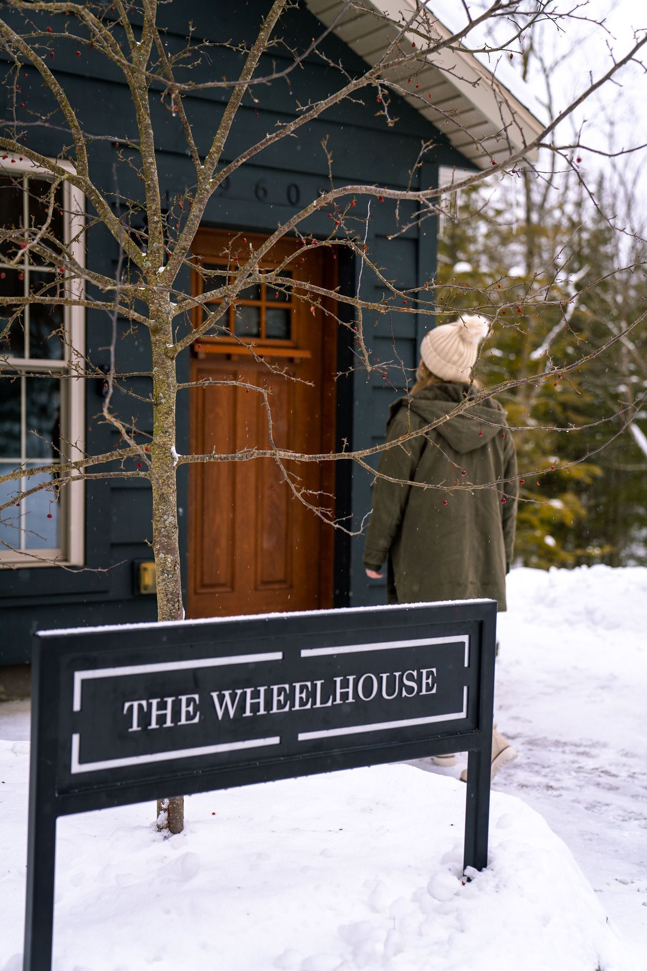 A sign for "The Wheelhouse" in front of a wooden building with a dark door and windows.