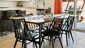 A modern kitchen with white cabinets, a dining area with black chairs, and a large window with blinds. - Red Cliffs PET FRIENDLY! (Washington)