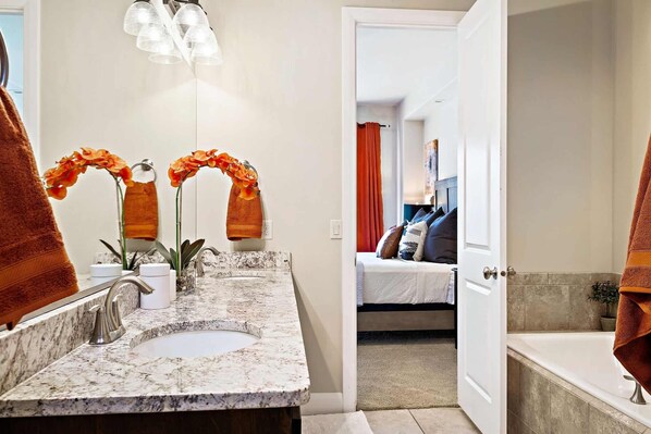 A bathroom with a marble sink, two mirrors, and orange orchids. There is a door leading to a bedroom with a bed and a nightstand. - Red Cliffs PET FRIENDLY! (Washington)