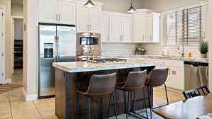 A modern kitchen with white cabinets, stainless steel appliances, a granite countertop, and bar stools. - Red Cliffs PET FRIENDLY! (Washington)