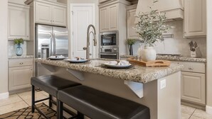 Una cocina moderna con armarios blancos, electrodomésticos de acero inoxidable, encimeras de granito y una isla central con asientos.