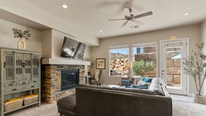 Una sala de estar con chimenea de piedra, un sofá grande, un televisor y un ventilador de techo.