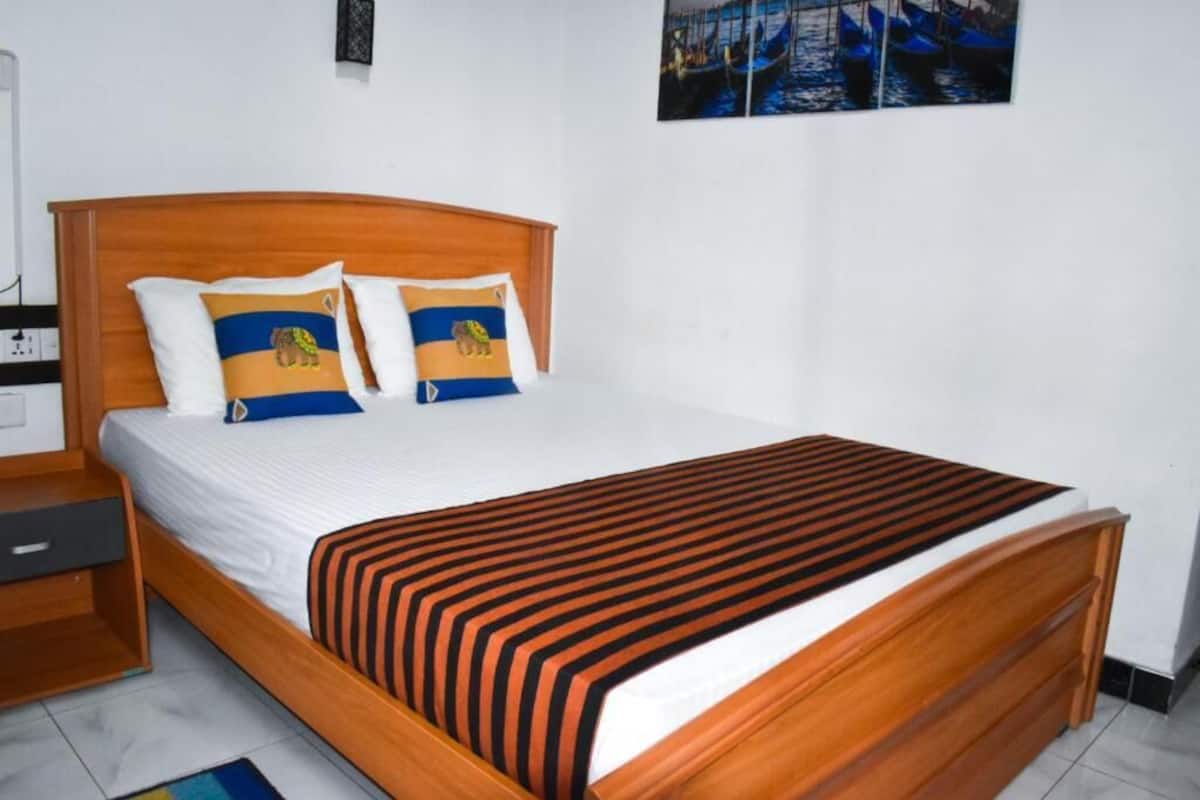 A neatly made bed with a striped blanket, two pillows with a lion design, and a wooden headboard.