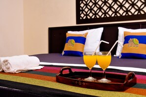 A neatly made bed with colorful striped bedding, a white towel, and a tray with two glasses of orange juice. - Myr-o Homestay (Anuradhapura)