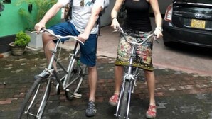 Two people on bicycles in a courtyard with a car and a building in the background. - Myr-o Homestay (Anuradhapura)
