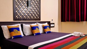 A bed with a striped bedspread, decorative pillows, and a rolled towel on the side. - Myr-o Homestay (Anuradhapura)