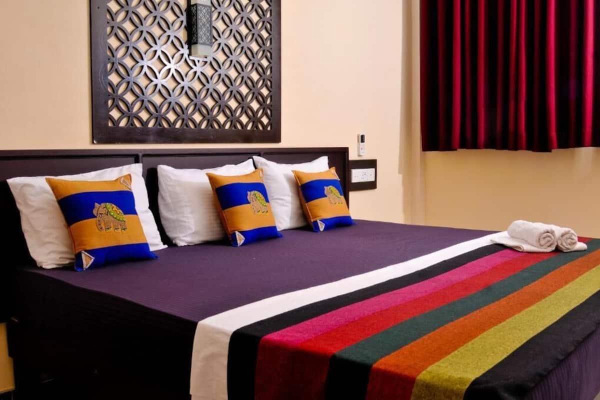 A bed with a striped bedspread, decorative pillows, and a rolled towel on the side.
