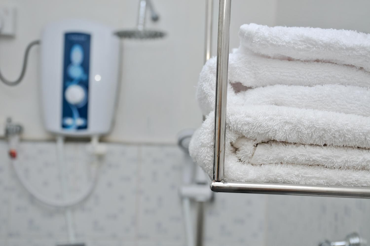 A bathroom with a towel rack holding neatly folded white towels, a handheld showerhead, and a wall-mounted water dispenser.