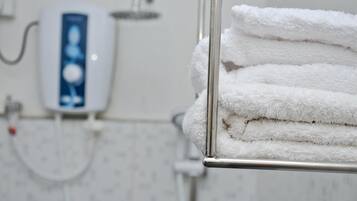 A bathroom with a towel rack holding neatly folded white towels, a handheld showerhead, and a wall-mounted water dispenser.