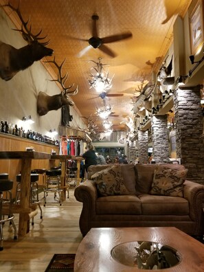 A room with a wooden ceiling, mounted animal heads, a bar area, and a couch.