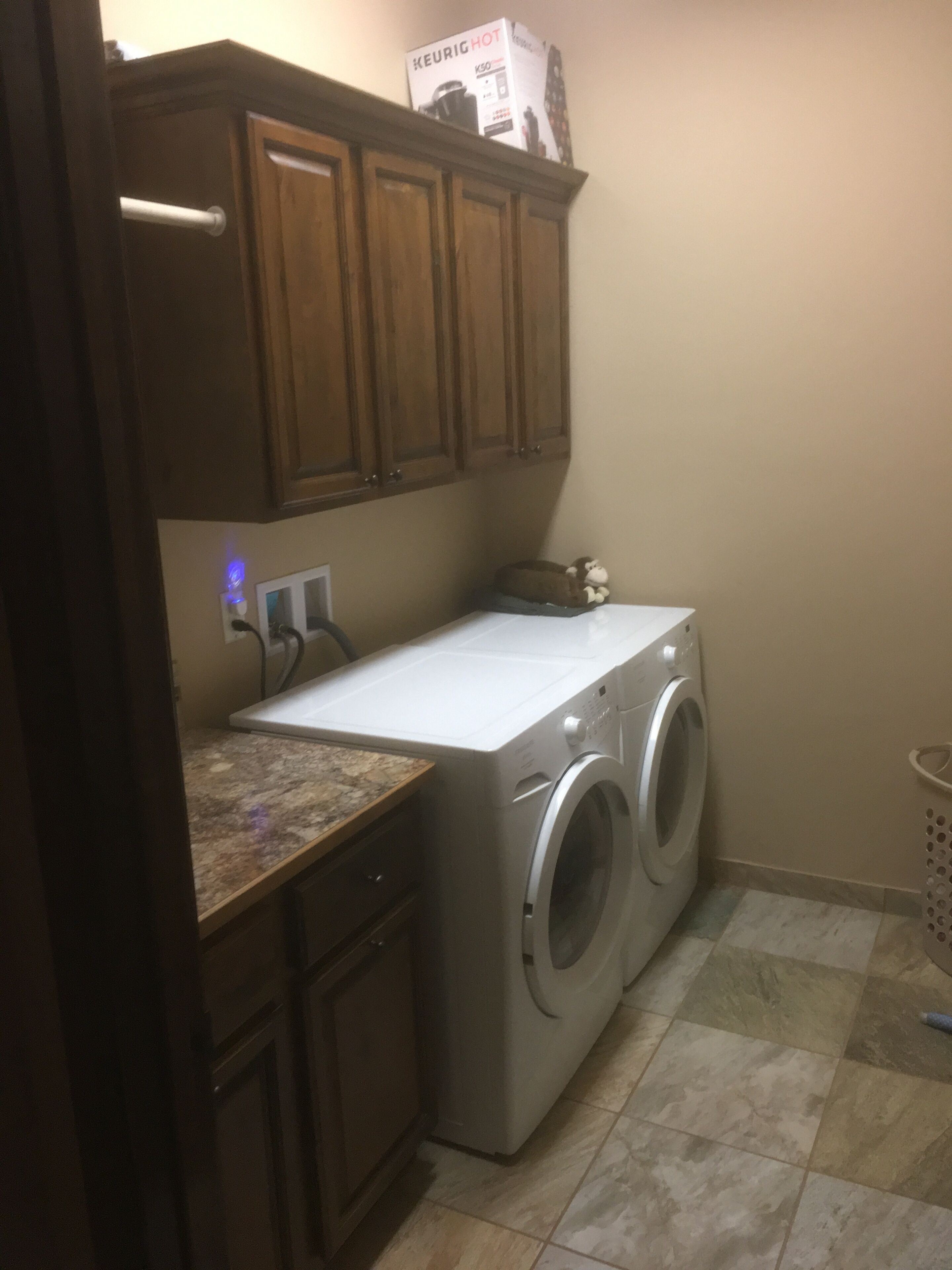 A laundry area with a front-loading washing machine and dryer, wooden cabinets, and a countertop.