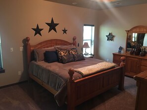 A bedroom with a wooden bed, a dresser, and a mirror. There are three stars on the wall and a window with blinds. - Big Log Cabin Home, Large Back Deck Overlooking Cedar Creek ~ Close To Downtown (Ruidoso)
